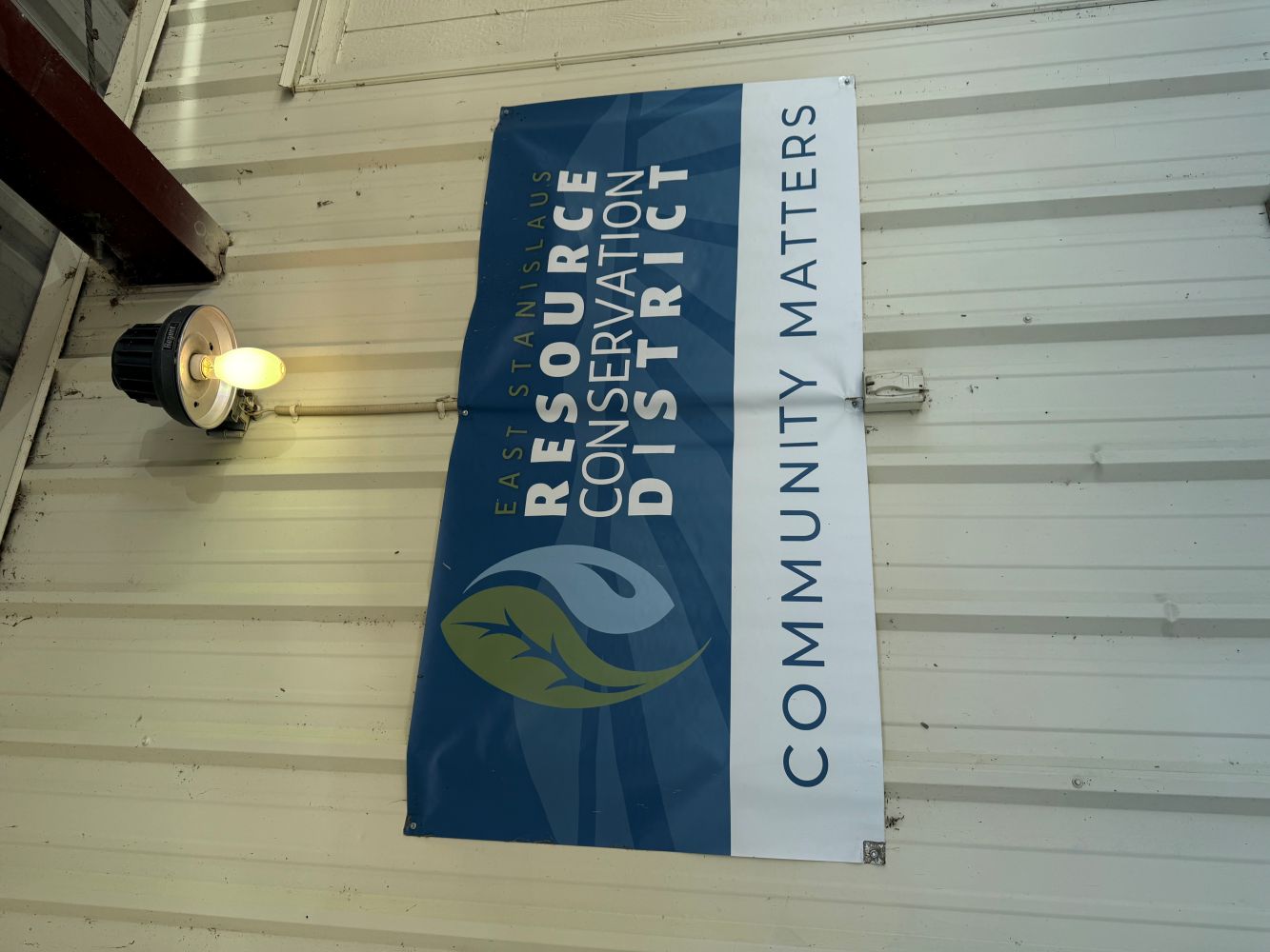 Sign: Resource Conservation District logo with 'Community Matters' on corrugated metal, lit by bulb